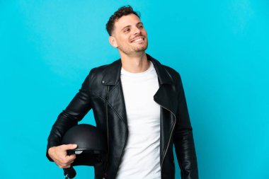 Motosiklet kasklı beyaz bir adam mavi arka planda izole edilmiş bir şekilde yukarı bakarken bir fikir düşünüyor.