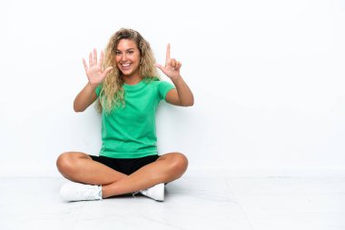 Yerde oturan kıvırcık saçlı kız yediyi parmaklarıyla sayıyor.