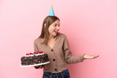 Elinde doğum günü pastası tutan Litvanyalı genç bir kadın. Pembe arka planda yalıtılmış.