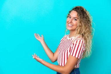 Mavi arka planda yalıtılmış kıvırcık saçlı kız, davet edilmek için ellerini yana uzatıyor.