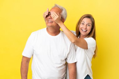 Orta yaşlı çift sarı arka planda izole edilmiş gözlerini kapayarak onu şaşırtıyor.