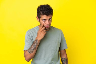 Sarı arka planda izole edilmiş yakışıklı Brezilyalı bir adam bir şey gösteriyor.