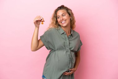 Kıvırcık saçlı kız pembe arka planda izole edilmiş hamile ve elinde emzik var.