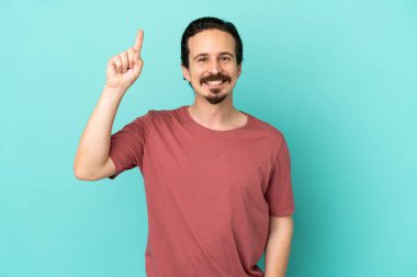 Mavi arka planda izole edilmiş genç beyaz adam harika bir fikre işaret ediyor.