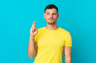 Beyaz tenli yakışıklı adam mavi arka planda izole edilmiş, şans diliyor ve en iyisini diliyor.