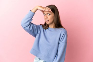 Soyutlanmış pembe arka planı olan genç bir kadın yan tarafa bakarken sürpriz jest yapıyor.