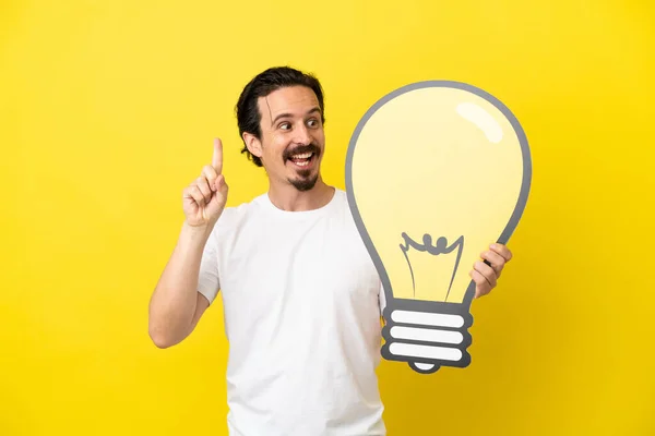 Young Caucasian Man Isolated Yellow Background Holding Bulb Icon Thinking — Stock Photo, Image