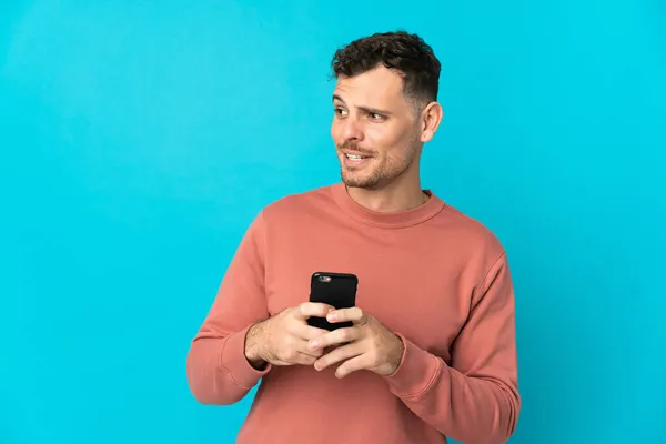 Junger Kaukasischer Gutaussehender Mann Isoliert Auf Blauem Hintergrund Mit Handy — Stockfoto