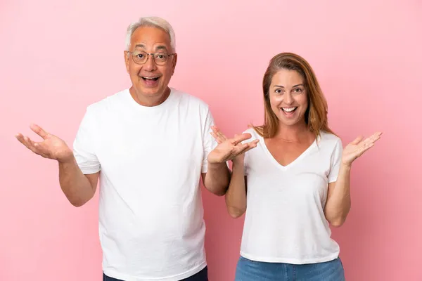 Middelaldrende Par Isolert Rosa Bakgrunn Med Overrasket Sjokkert Ansiktsuttrykk – stockfoto