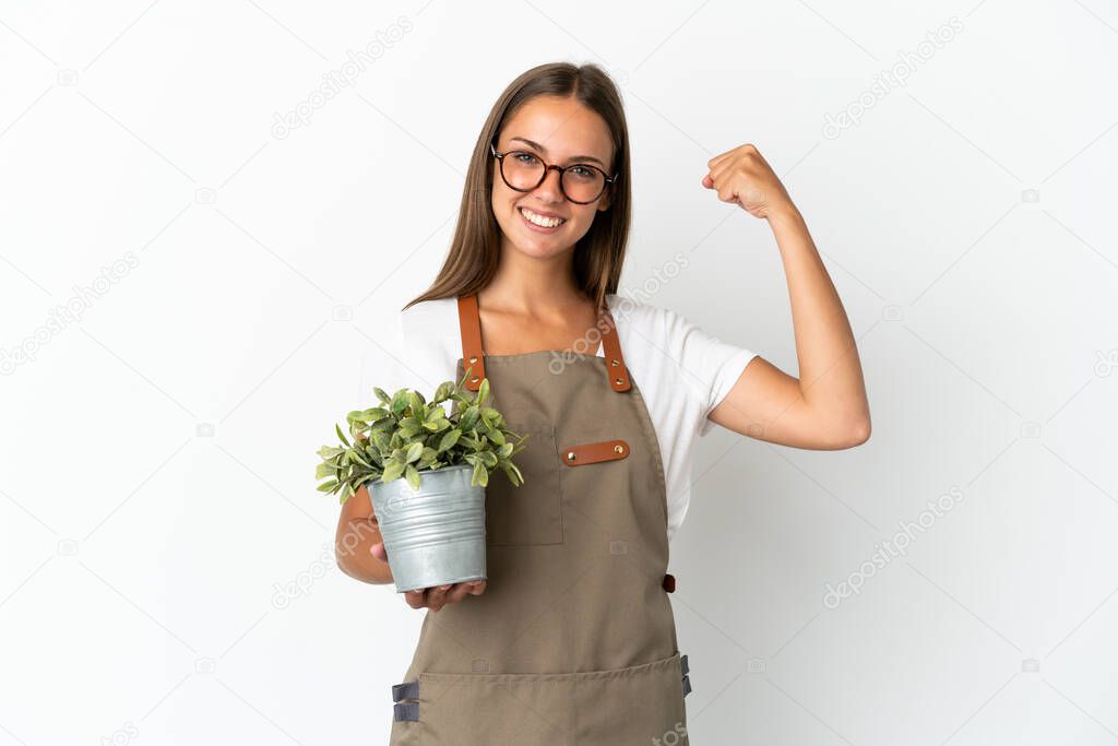 Gardener girl holding a plant over isolated white background doing strong gesture