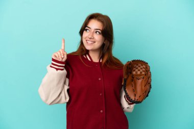 Beyzbol oynayan genç kızıl saçlı kadın mavi arka planda izole edilmiş. Harika bir fikre işaret ediyor.