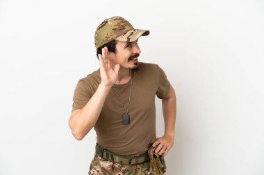 Asker adam beyaz arka planda izole edilmiş bir şekilde bir şeyler dinlerken elini kulağına koyar.