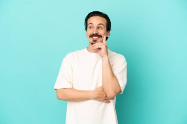 Kafkasyalı genç adam mavi arka planda izole edilmiş bir şekilde yukarı bakarken bir fikir düşünüyor.