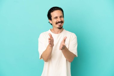 Mavi arka planda izole edilmiş genç beyaz adam bir konferansta sunumdan sonra alkışlıyor.