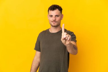 Sarı arka planda izole edilmiş beyaz, yakışıklı bir adam parmağını kaldırıyor ve gösteriyor.