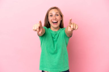 Pembe arka planda izole edilmiş genç İngiliz kadın şaşırmış ve ön tarafı işaret ediyor.
