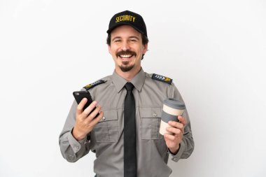 Beyaz arka planda izole edilmiş beyaz bir güvenlik görevlisi elinde kahve ve bir cep telefonu tutuyor.