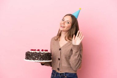 Elinde doğum günü pastası tutan Litvanyalı genç bir kadın pembe arka planda izole edilmiş mutlu bir ifadeyle selamlıyor.
