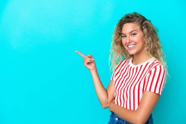 Mavi arka planda izole edilmiş kıvırcık saçlı kız parmağını yana doğru gösteriyor.