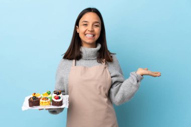 Pasta şefi büyük bir pasta tutuyor. Mavi arka plan üzerinde. Fotokopi alanı hayali bir şey tutuyor..