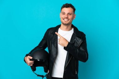 Mavi arka planda izole edilmiş motosiklet kasklı beyaz bir adam bir ürünü sunmak için kenarı işaret ediyor.