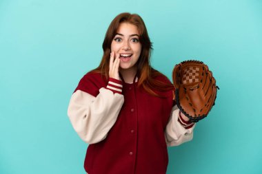 Beyzbol oynayan genç kızıl saçlı kadın mavi arka planda izole edilmiş, şaşırmış ve şok olmuş bir yüz ifadesi var.