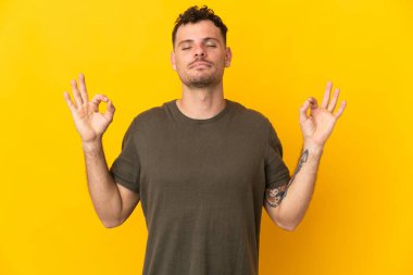 Zen pozisyonunda sarı arka planda izole genç beyaz yakışıklı adam.