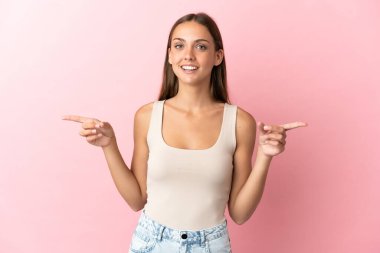 Soyutlanmış pembe arka planda genç bir kadın parmak uçlarını işaret ediyor ve mutlu.