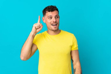 Genç, beyaz, yakışıklı bir adam mavi arka planda izole edilmiş. Çözümü bulmak için parmağını kaldırıyor.