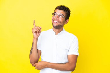 Sarı arka planda izole edilmiş yakışıklı Brezilyalı adam harika bir fikre işaret ediyor.