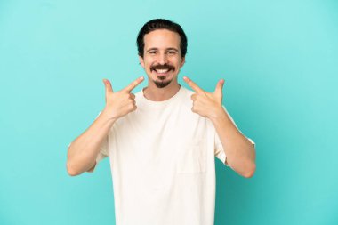 Kafkasyalı genç adam mavi arka planda izole edilmiş bir şekilde baş parmak işareti yapıyor.