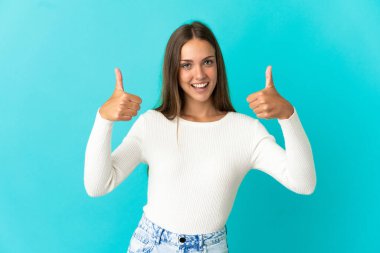 Soyutlanmış mavi arka planda genç bir kadın baş parmak işareti yapıyor.