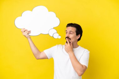 Sarı arka planda izole edilmiş genç beyaz bir adam düşünme balonu tutuyor.