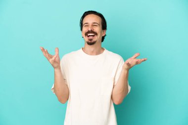 Kafkasyalı genç adam mavi arka planda izole edilmiş, çok gülümsüyor.