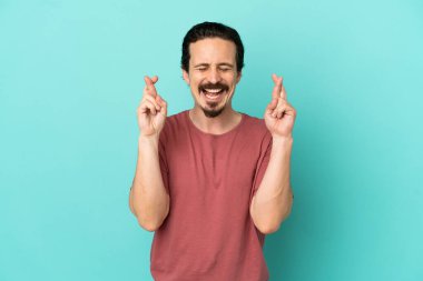 Genç beyaz adam mavi arka planda izole edilmiş ve şans diliyor.