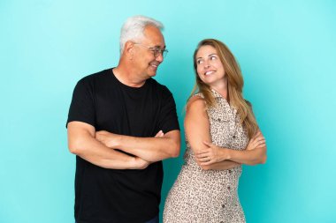 Mavi arka planda izole edilmiş orta yaşlı bir çift, gülümseyerek omuzlarının üzerinden bakıyor.