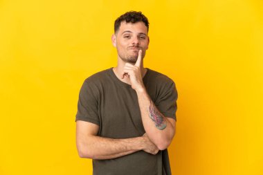 Beyaz tenli yakışıklı adam sarı arka planda izole edilmiş ve düşünüyor.