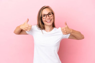 Pembe arka planda izole edilmiş genç bir İngiliz kadın baş parmak işareti yapıyor.
