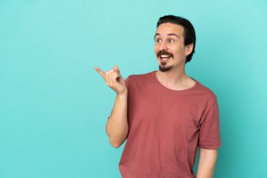 Kafkasyalı genç adam mavi arka planda izole edilmiş bir şekilde parmağını kaldırarak çözümü anlamaya çalışıyor.