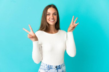 İzole edilmiş mavi arka planda genç bir kadın zafer işaretini iki eliyle gösteriyor.