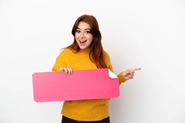 Beyaz arka planda izole edilmiş genç kızıl saçlı bir kadın boş bir levha tutuyor ve işaret ediyor.