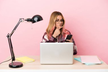 Pembe arka planda dizüstü bilgisayarı olan genç bir bayan iş yerinde düşünüyor ve bir mesaj gönderiyor.