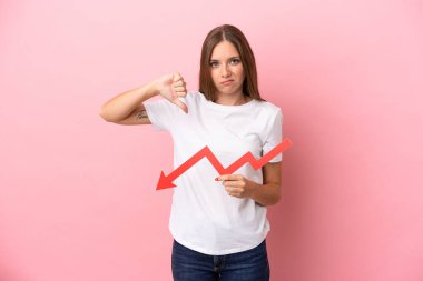 Genç Litvanyalı bir kadın pembe arka planda izole edilmiş, aşağıya doğru ok atıyor ve kötü sinyal veriyor.