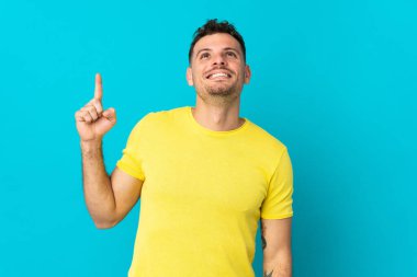 Kafkasyalı yakışıklı genç adam mavi arka planda izole edilmiş yukarı bakıyor ve şaşırıyor.