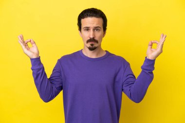 Zen pozisyonunda sarı arka planda izole edilmiş genç beyaz adam.