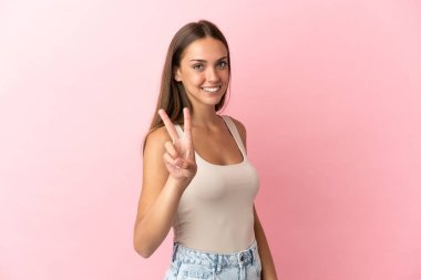 Soyutlanmış pembe arka planda genç bir kadın gülümsüyor ve zafer işareti gösteriyor
