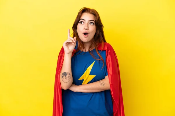 stock image Super Hero redhead woman isolated on yellow background thinking an idea pointing the finger up