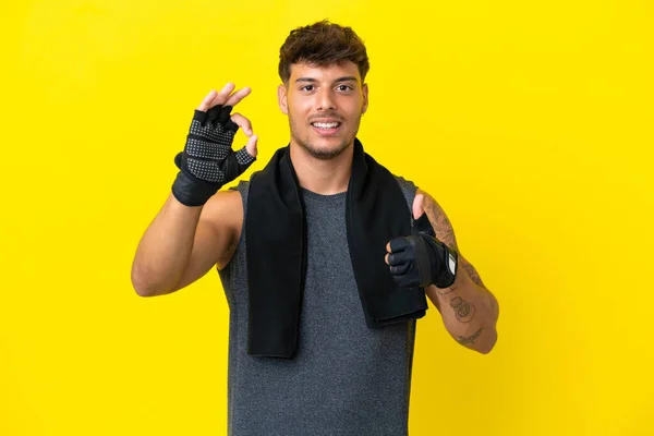 年轻的体育高加索男子与毛巾隔离黄色背景显示好迹象和大拇指向上的姿态 — 图库照片