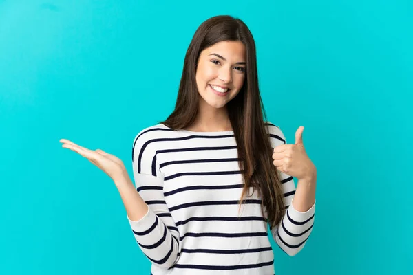 十代のブラジル人の女の子以上隔離された青の背景を保持コピースペース想像上のヤシの上に挿入する広告と親指アップ — ストック写真