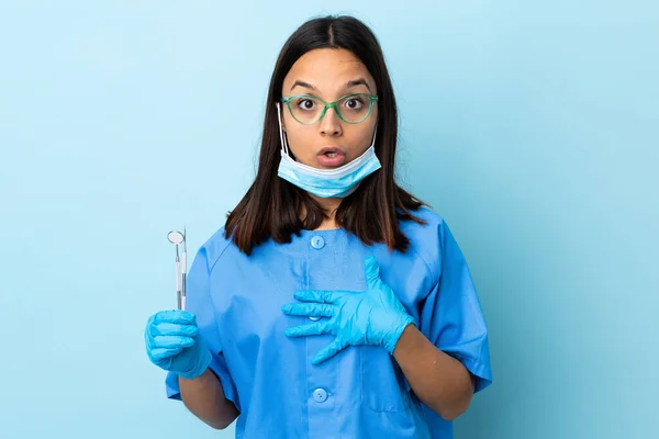 年轻的黑发混血女牙医拿着工具站在孤立的背景下 看着右边 惊讶而震惊 — 图库照片